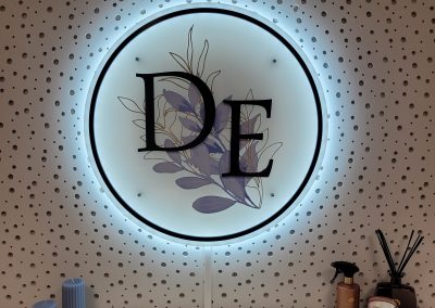 Enseigne lumineuse ronde rétroéclairée avec les initiales DE et un motif de feuilles, réalisée par Ardesca Print