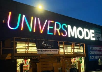 Pose et installation de l'enseigne lumineuse multicolore Univers Mode par Ardesca Print, photographiée de nuit avec une nacelle élévatrice