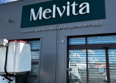 Enseigne Melvita réalisée par Ardesca Print, avec lettres en relief sur fond vert et mention cosmétique bio née en Ardèche en 1983