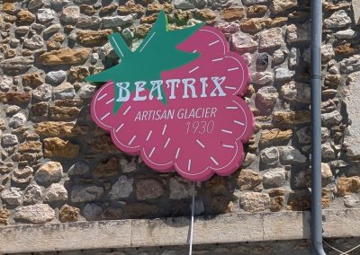Enseigne en forme de framboise rose et verte pour Beatrix, Artisan Glacier depuis 1930, fixée sur un mur en pierre