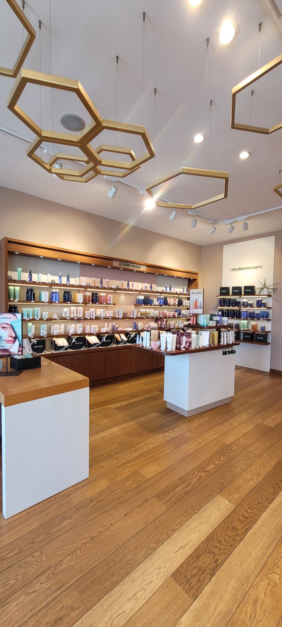 Plafond de la boutique Melvita apres habillage, suspensions hexagonales dorees et murs clairs
