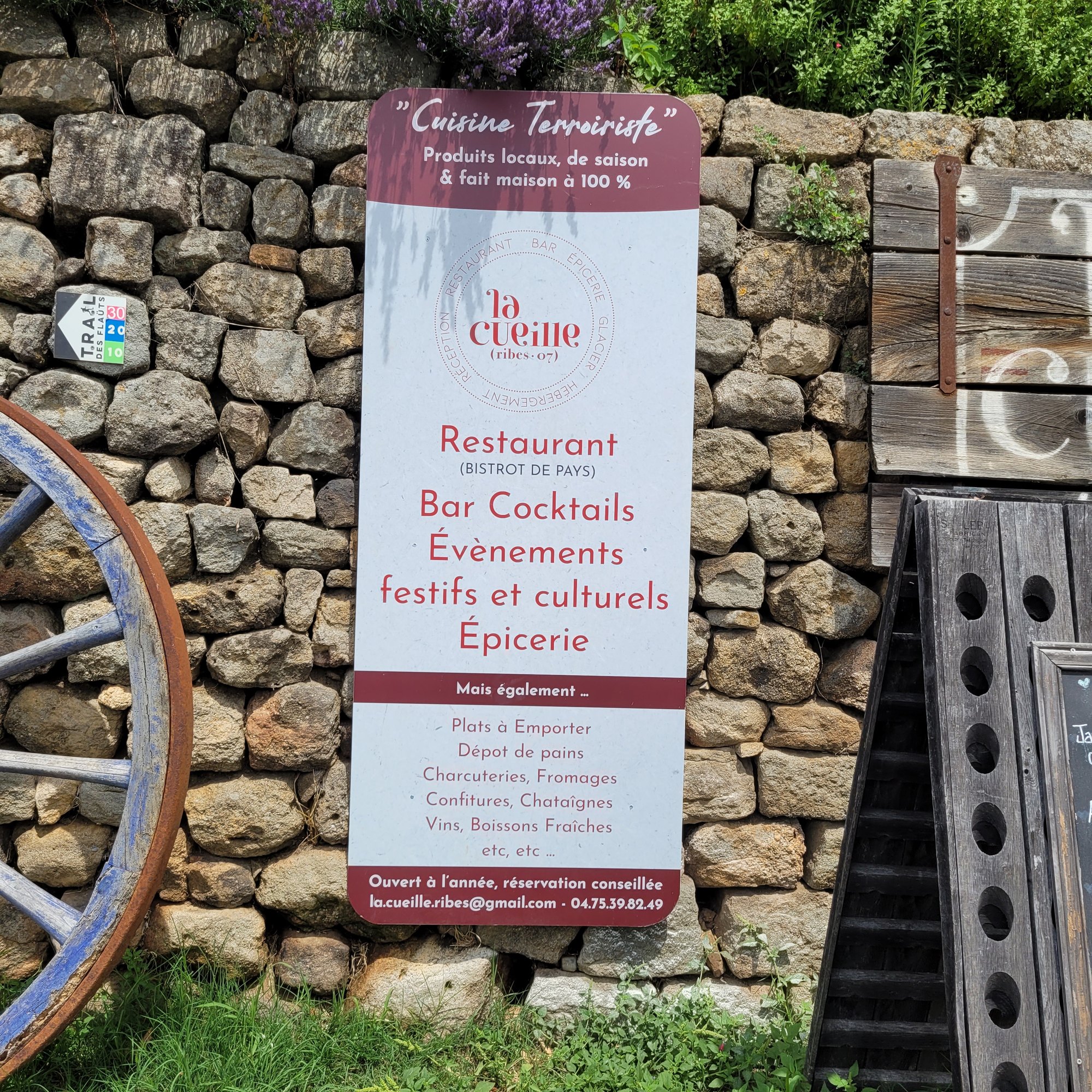 Grand panneau imprimé du restaurant La Cueille à Ribes, à coins arrondis, adossé à un mur de pierre sèche