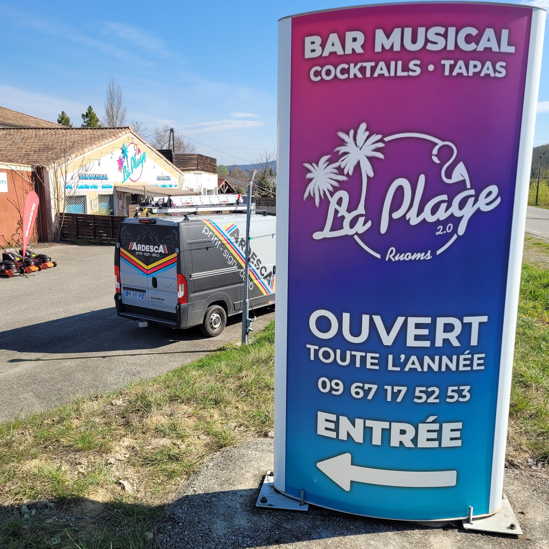 Totem lumineux courbe du bar musical La Plage à Ruoms, en dégradé magenta et bleu, installé en bord de route