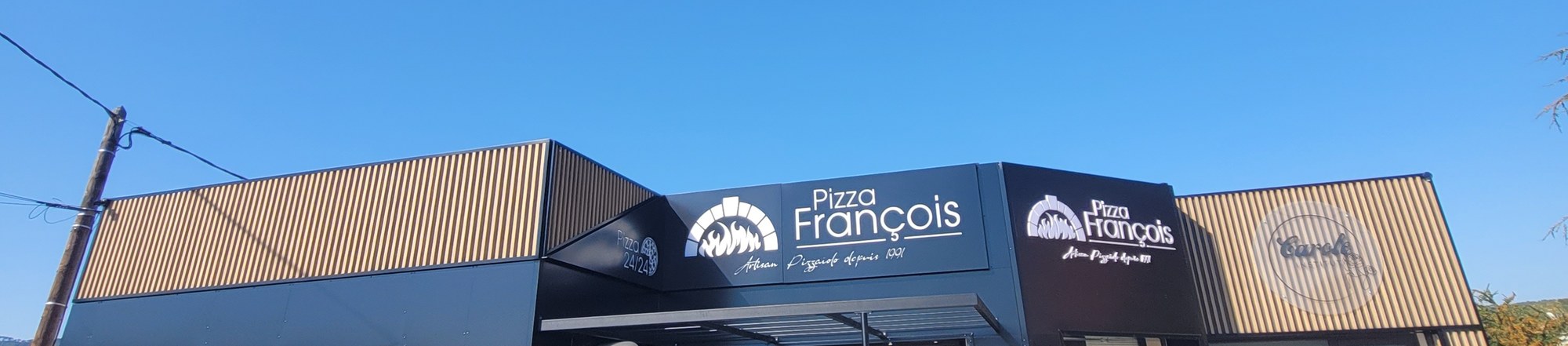 Bandeau d'enseigne Pizza François en lettres blanches sur panneau noir, sur une façade en bardage noir et bois