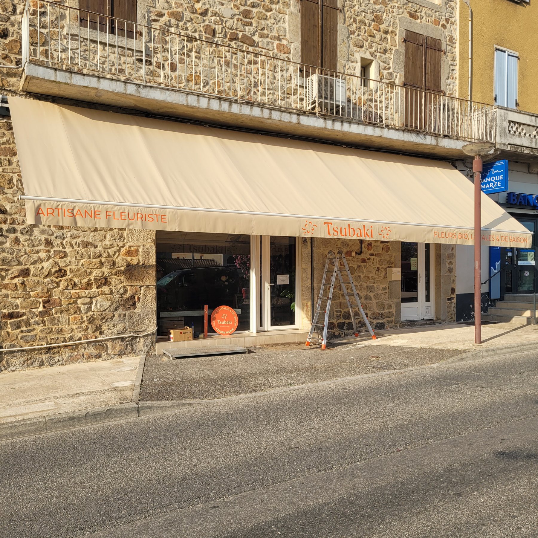 Store banne beige de l'atelier floral Tsubaki, avec le lettrage orange Artisane fleuriste et Fleurs bio locales et de saison, sur une façade en pierre