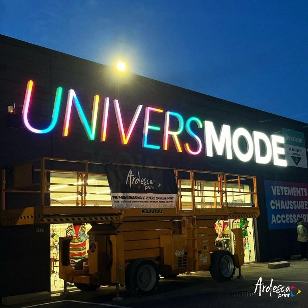 Enseigne UniversMode en lettres boîtier lumineuses au crépuscule, le mot UNIVERS en dégradé arc-en-ciel piloté en LED DMX