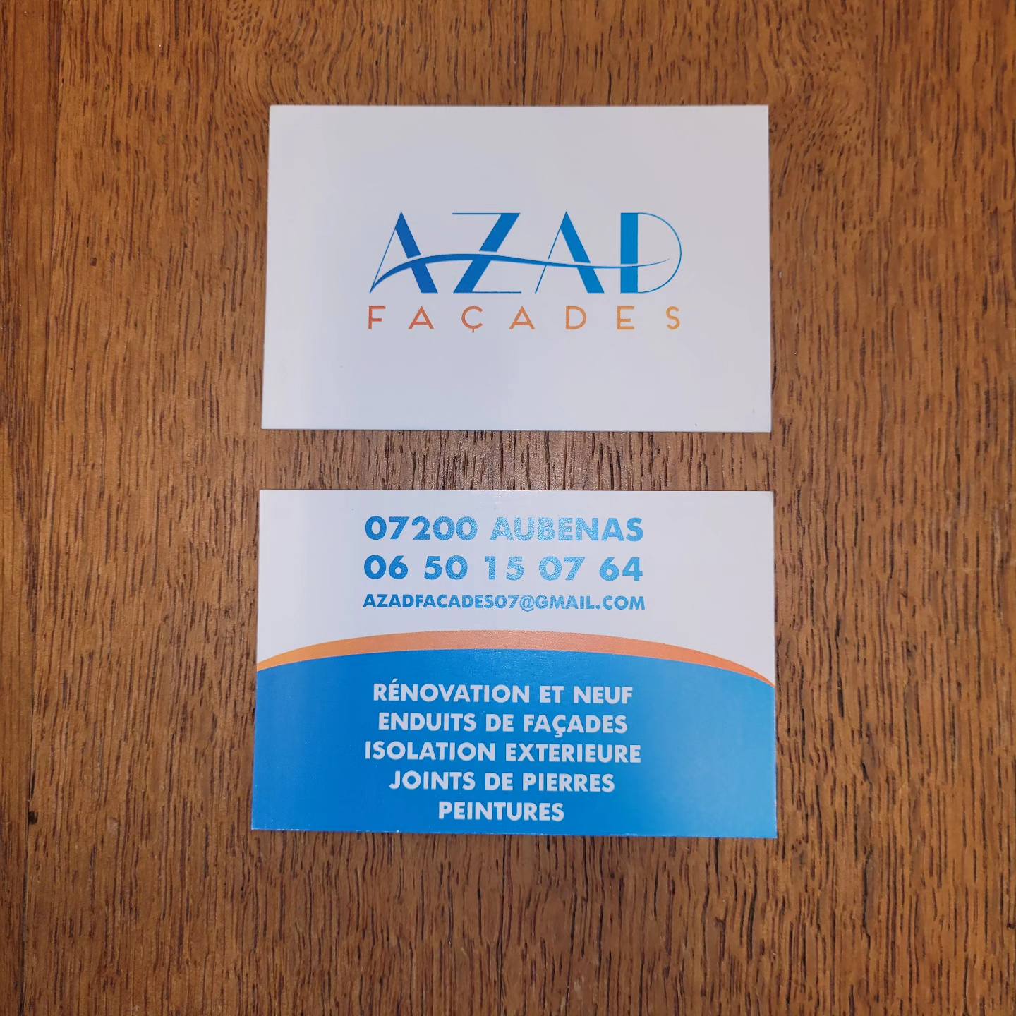 Recto et verso des cartes de visite AZAD Façades à Aubenas, rénovation et enduits de façades, posées sur un plateau en bois