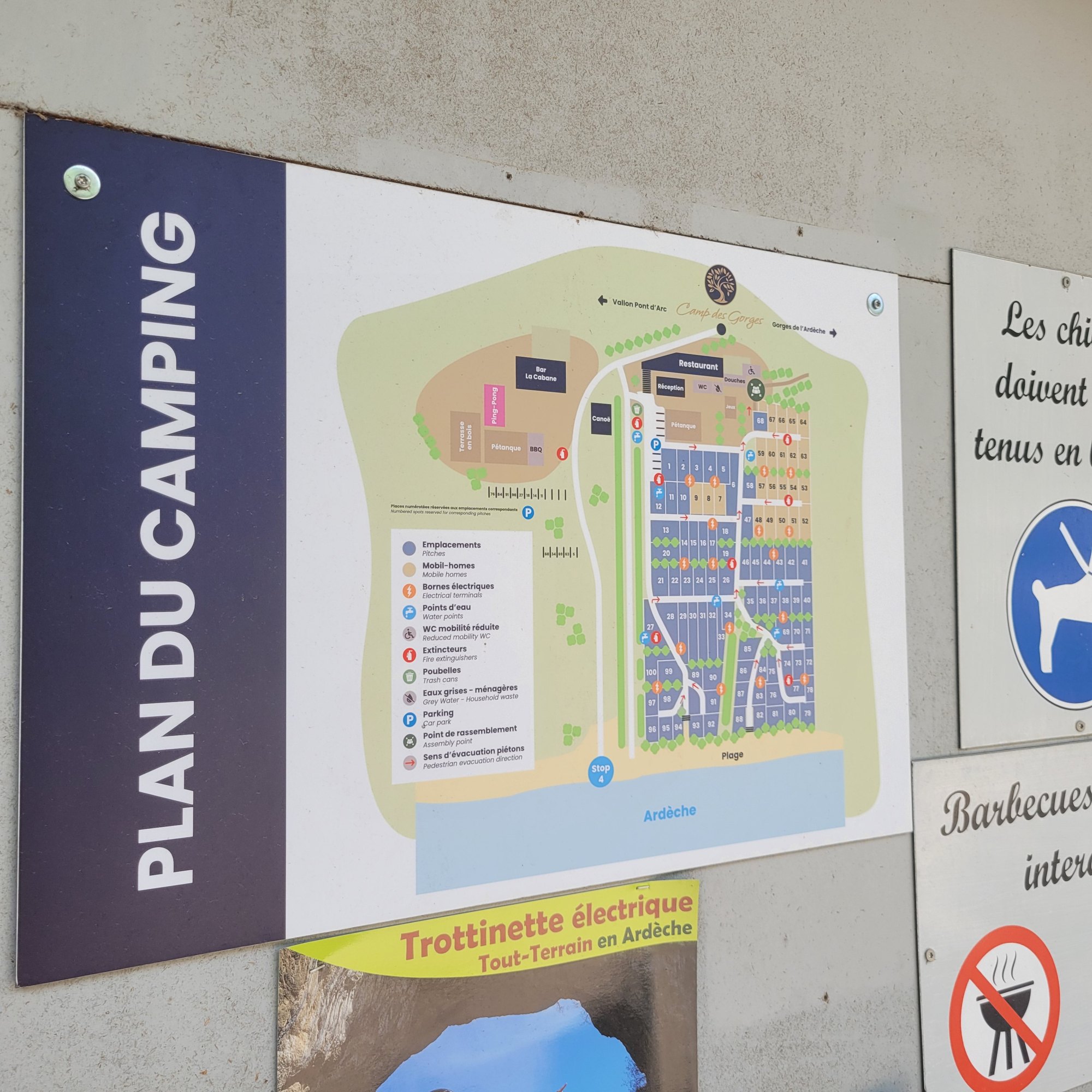 Panneau mural imprimé intitulé Plan du camping, présentant le plan général du site avec une légende de pictogrammes pour les emplacements, les points d'eau, les extincteurs et le point de rassemblement