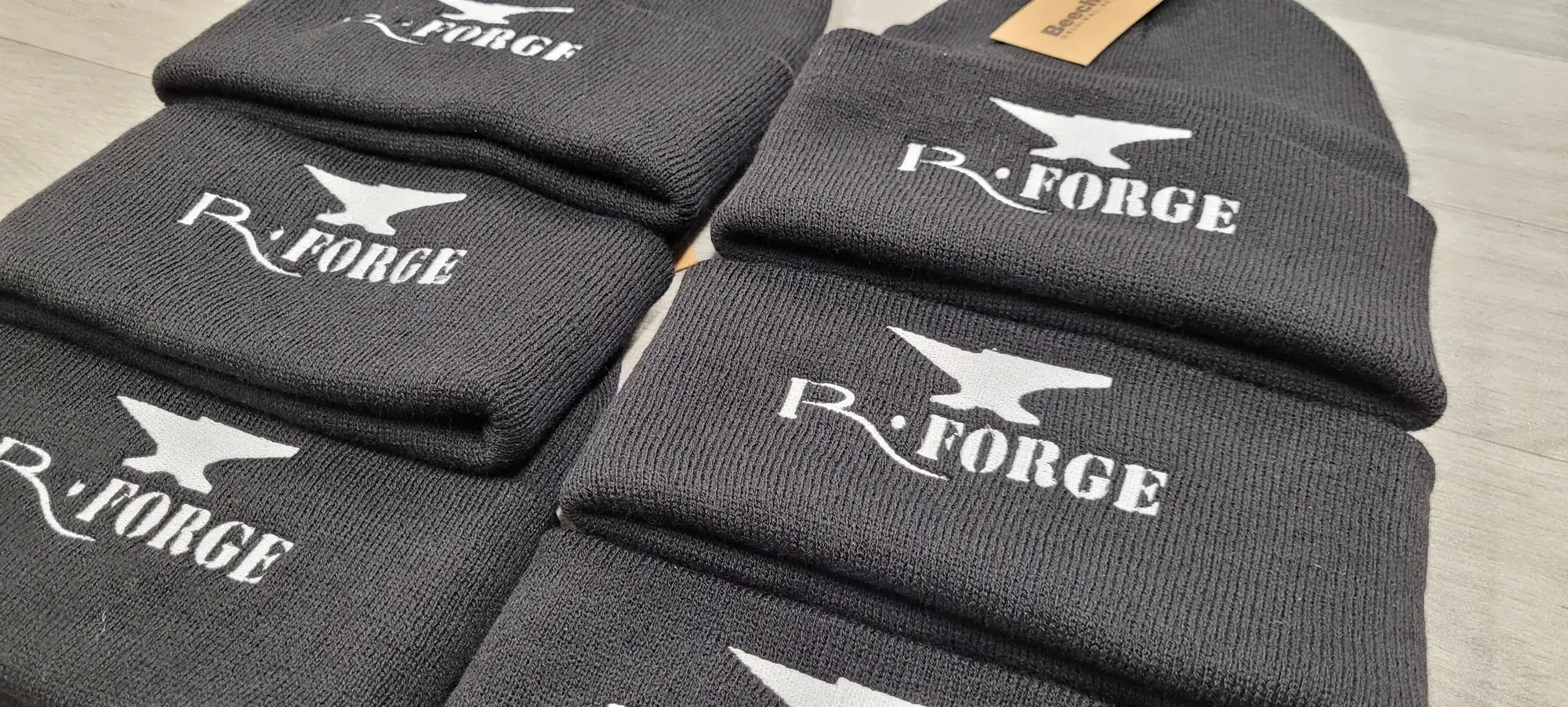 Six bonnets en maille anthracite alignés, brodés en fil blanc du logo R-Forge