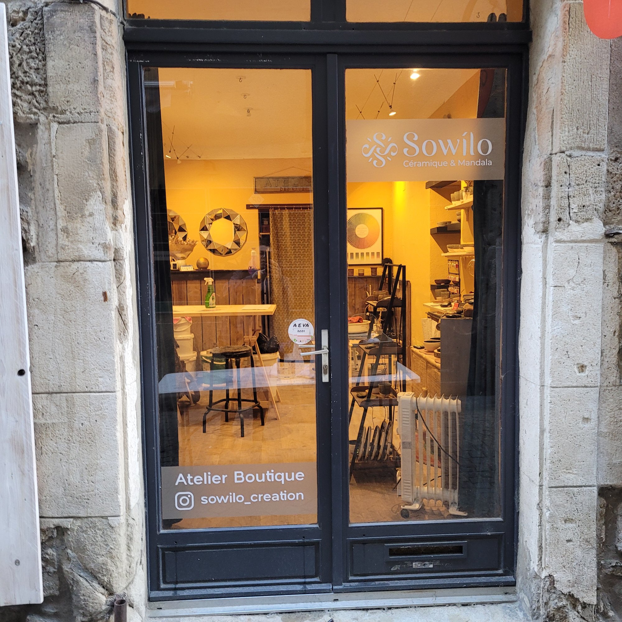 Porte vitrée d'une boutique d'artisan céramiste, avec un bandeau adhésif portant le logo et l'activité en haut du vitrage, et la mention Atelier Boutique avec le compte Instagram en bas