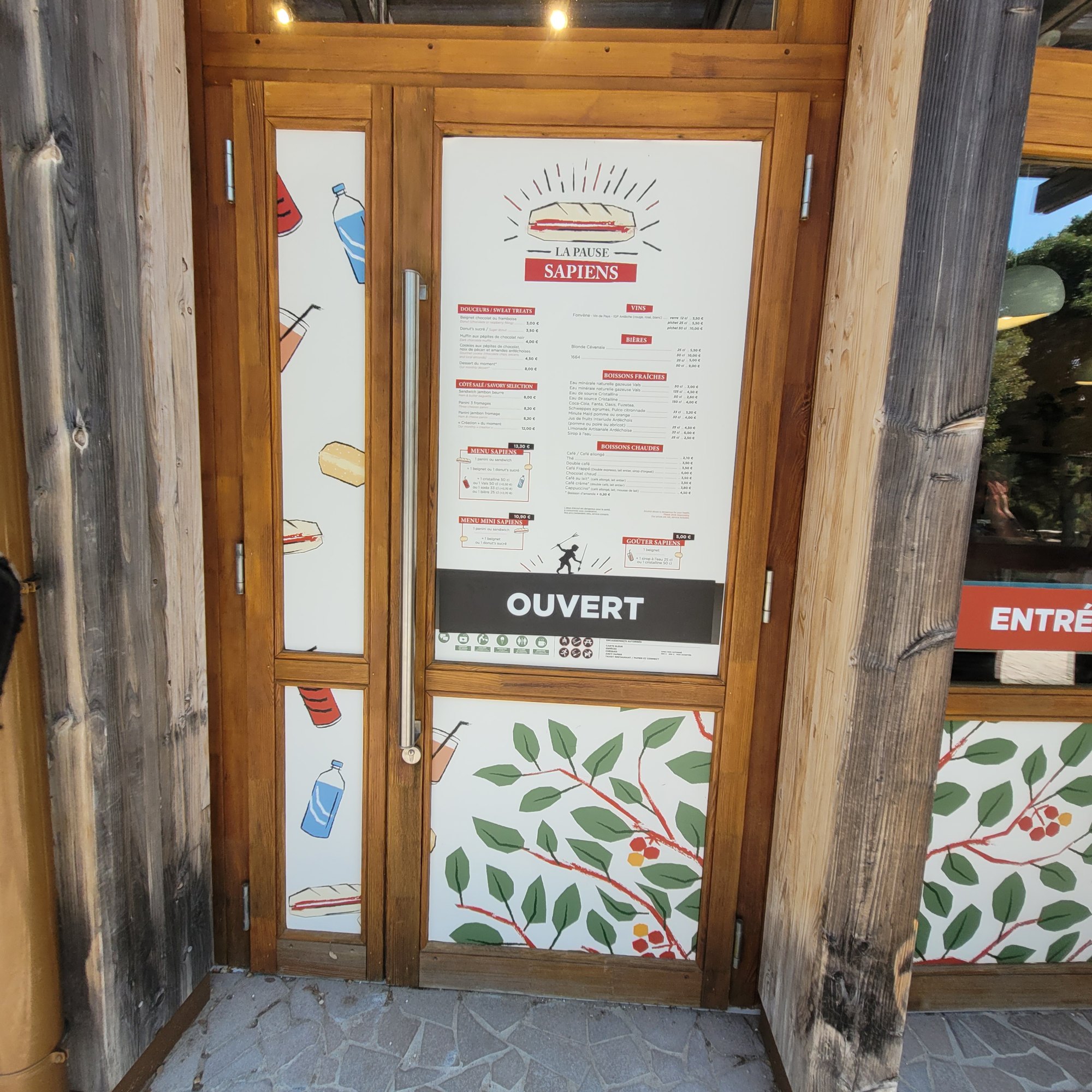 Porte vitrée d'un point de restauration entièrement habillée en adhésif : carte des menus imprimée sur le vantail, bandeau OUVERT, décor de feuillages sur les parties basses et vitrages latéraux illustrés