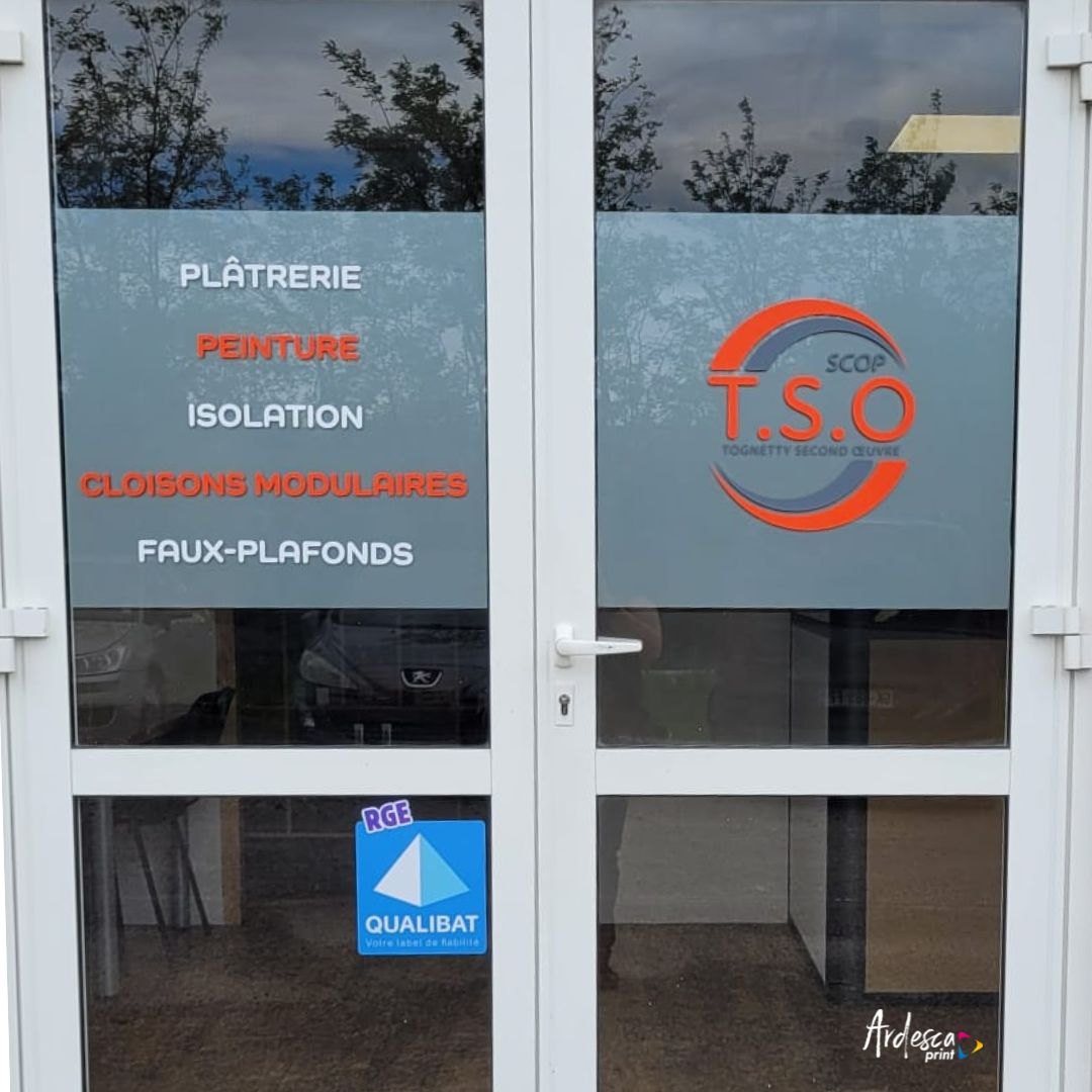 Porte double vitrée dont les panneaux hauts portent en adhésif la liste des prestations — plâtrerie, peinture, isolation, cloisons modulaires, faux-plafonds — et le logo de l'entreprise