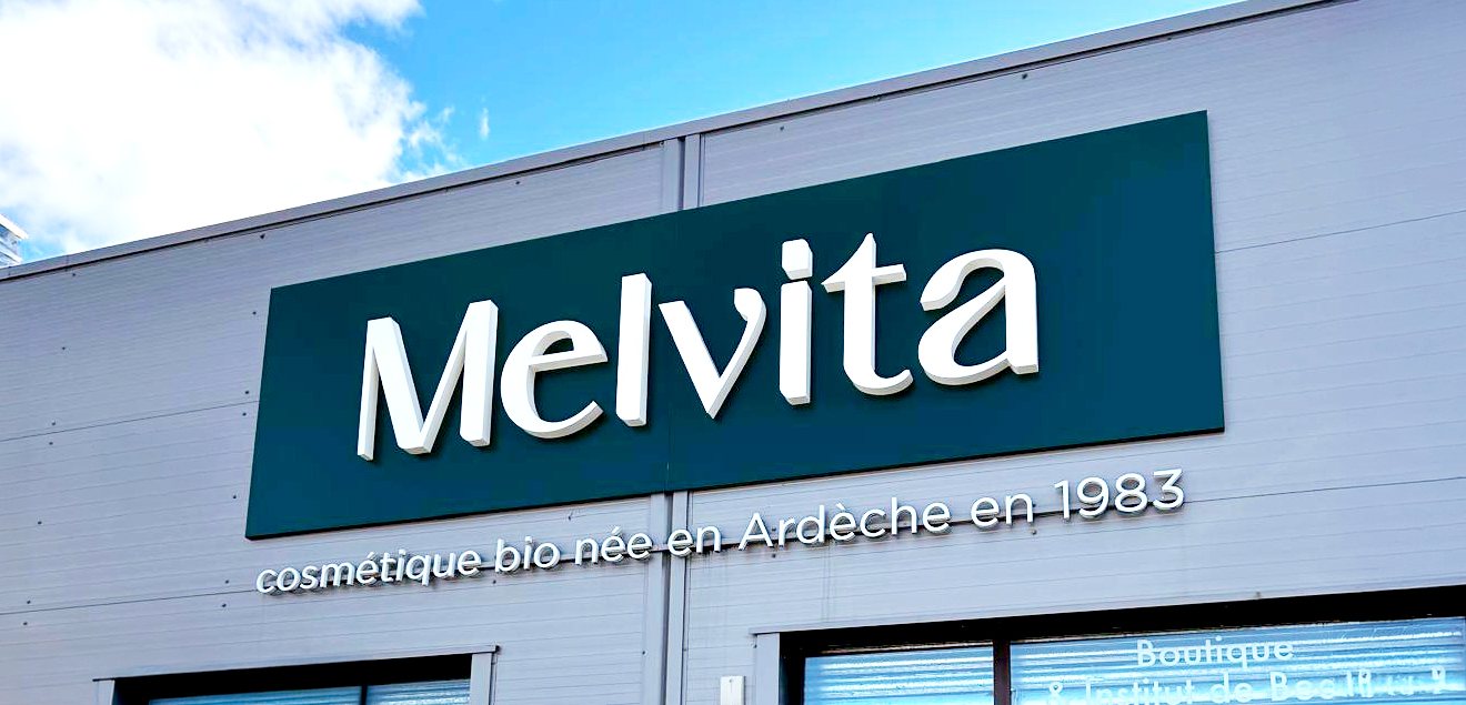 Enseigne Melvita : lettres relief blanches sur bandeau vert et lettrage « cosmétique bio née en Ardèche en 1983 »